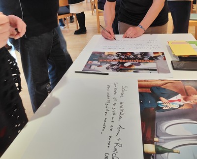 Ein Plakat liegt auf einem Tisch, jemand schreibt darauf. In Handschrift steht: "Schere zwischen Arm und Reich"