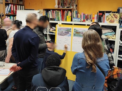 Menschen stehen um ein Plakat, eine Person schreibt darauf.